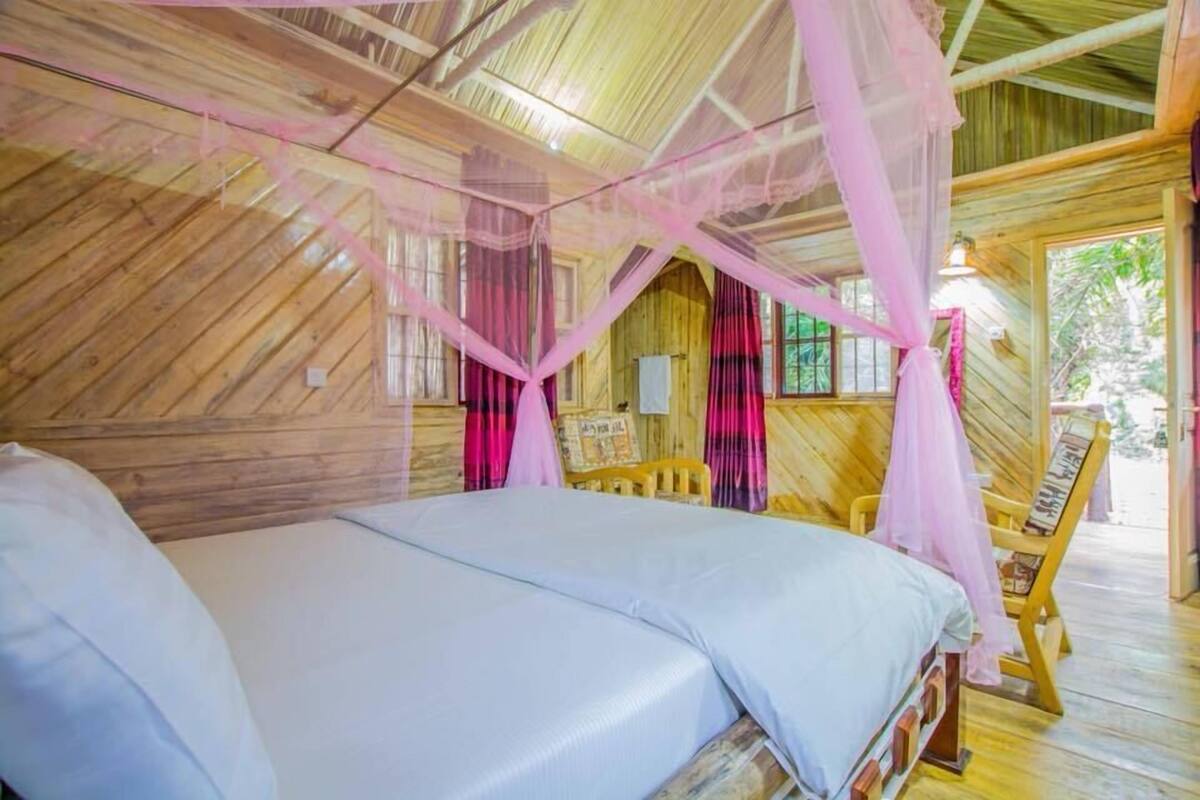A wooden room with a bed, a chair, and a window.