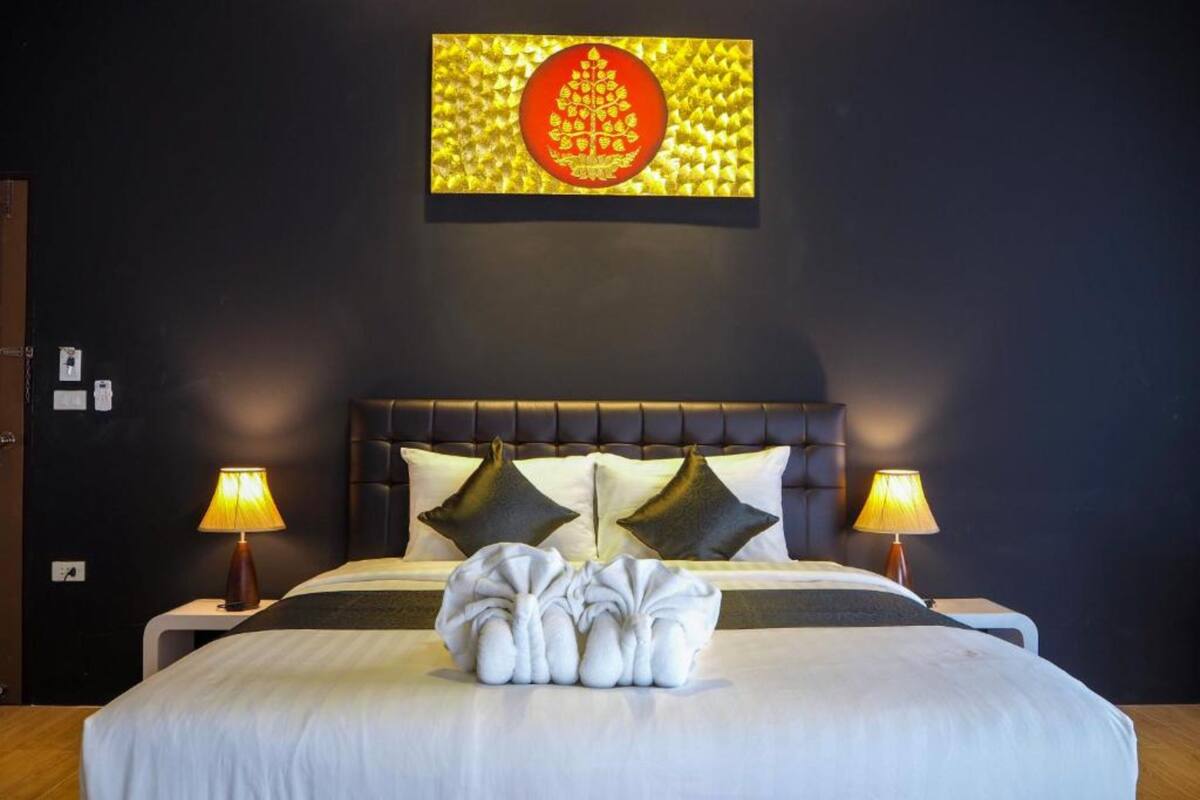 A hotel room with a large bed, two bedside lamps, a headboard with a geometric pattern, and a wall-mounted artwork.