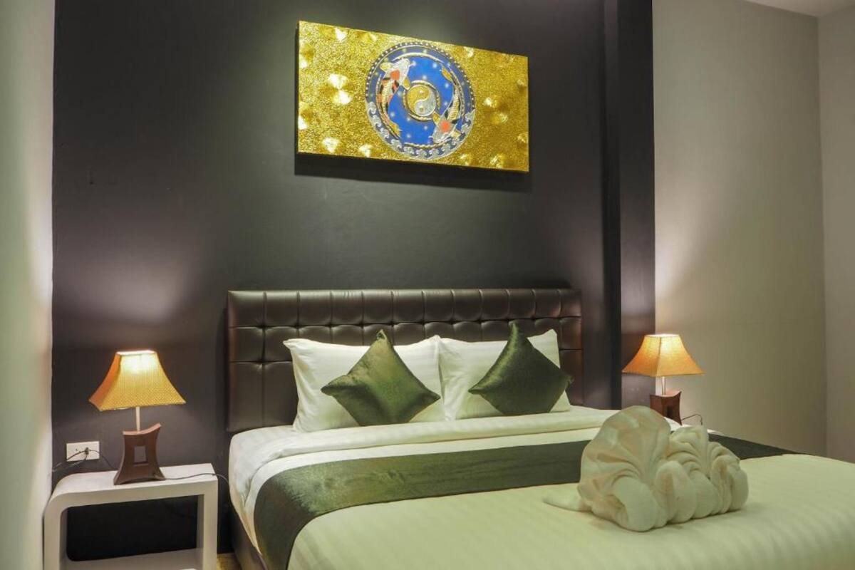 A hotel room with a dark wall, a bed with green and white bedding, two bedside lamps, and a decorative pillow.