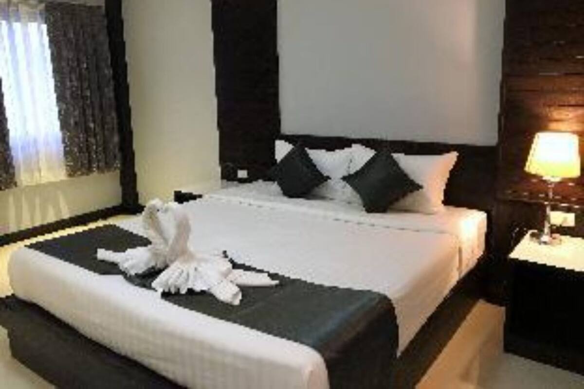 A hotel room with a large bed, a bedside table with a lamp, and a window with curtains.