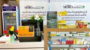 A pharmacy counter with a reception sign, a vase with flowers, and shelves stocked with various medications. - The residence (Koh Samui)