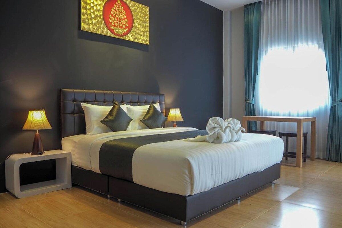 Ein modernes Hotelzimmer mit einem großen Bett, zwei Nachttischlampen, einem kleinen Tisch und einem großen Fenster mit Vorhängen.