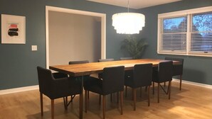 A dining area with a wooden table and black chairs, a white door, a potted plant, and a window with blinds.