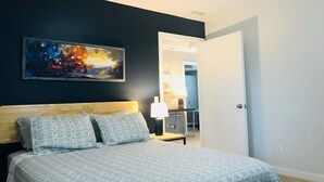 A bedroom with a bed, a nightstand, a lamp, and a painting on the wall.