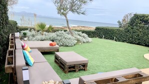 A wooden deck with outdoor seating, a small table with a basket, and a view of the ocean. - EMBAT - Seafront house with garden, pool and bbq. (Colonia San Pedro)