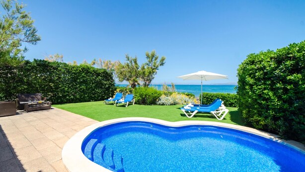 A swimming pool with a view of the sea, surrounded by a well-maintained lawn and a few lounge chairs. - EMBAT - Seafront house with garden, pool and bbq. (Colonia San Pedro)