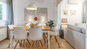 A modern dining area with a wooden table, white chairs, and a central light fixture. There is a plant on the table and a lamp on the side. - EMBAT - Seafront house with garden, pool and bbq. (Colonia San Pedro)