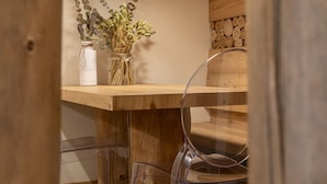 Una mesa de comedor de madera con una silla de vidrio transparente, una lámpara colgante y un jarrón con plantas secas.
