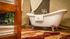 A bathroom with a freestanding bathtub, a wooden floor, and a patterned rug. - Ntoroko Game Lodge (Ntoroko)