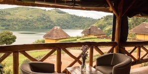 A rustic wooden structure with a thatched roof overlooking a lake and hills. - Ntoroko Game Lodge (Ntoroko)