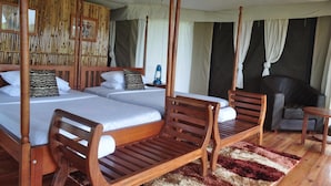 A four-poster bed with two wooden chairs, a small table, and a nightstand with a lantern. - Ntoroko Game Lodge (Ntoroko)