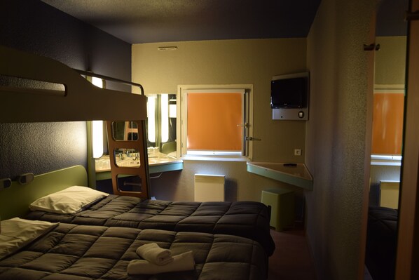 A hotel room with bunk beds, a desk, a chair, a television, and a window with curtains.
