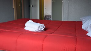 A red bed with a neatly folded white towel and a white pillow. - Hotel Design Booking (Villeneuve-le-Roi)