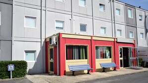 A building with a red and beige facade, a wheelchair accessibility sign, and two benches outside. - Hotel Design Booking (Villeneuve-le-Roi)