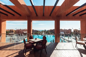 Terraza con vista a la piscina, mobiliario de madera y cielo despejado.