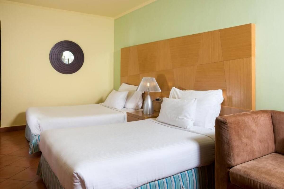 Hotellihuone, jossa on kaksi sänkyä, puinen pääty, pyöreä peili ja ruskea nojatuoli.