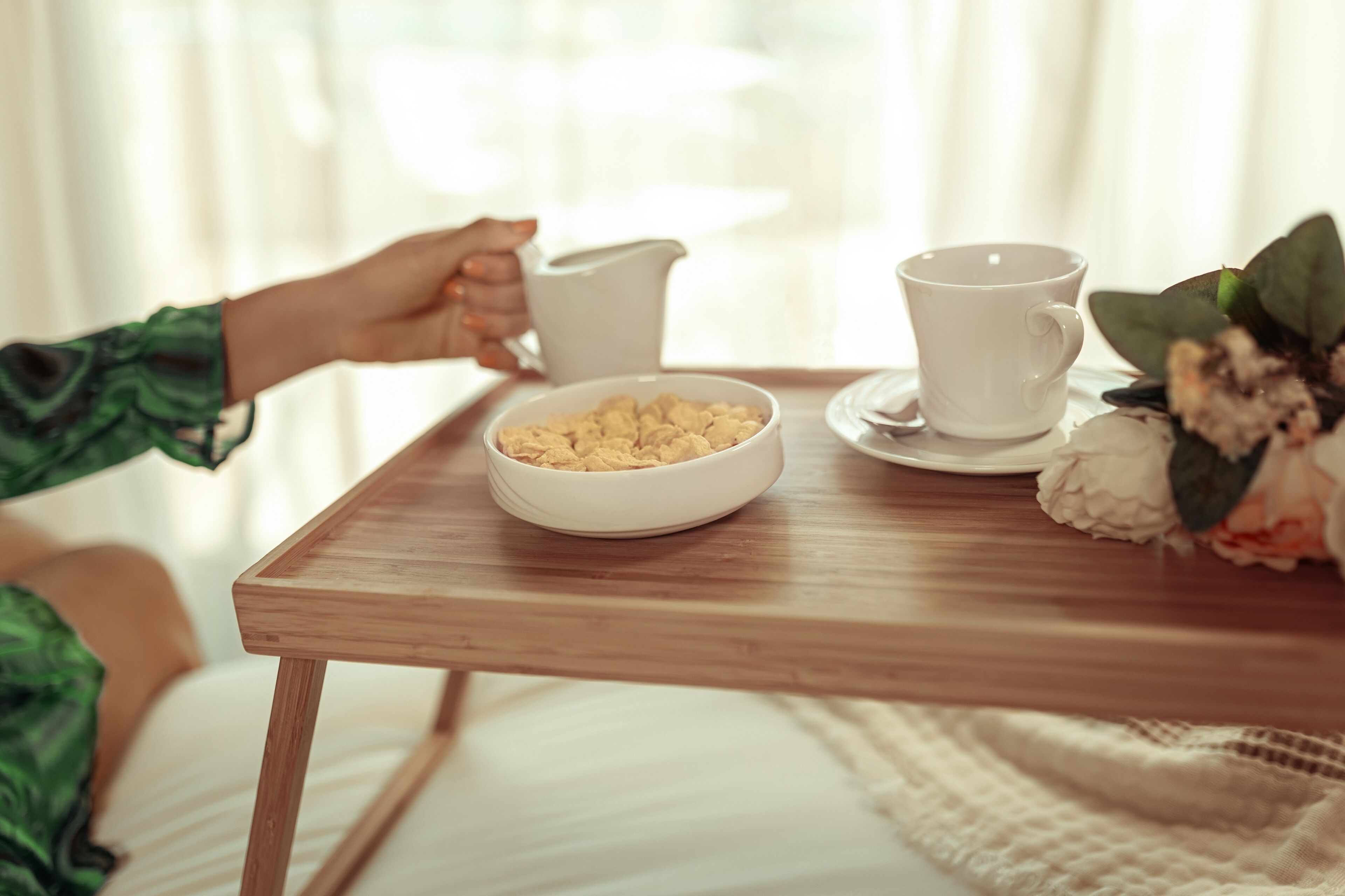 A wooden table with a bowl of cereal, a white pitcher, and a white cup.