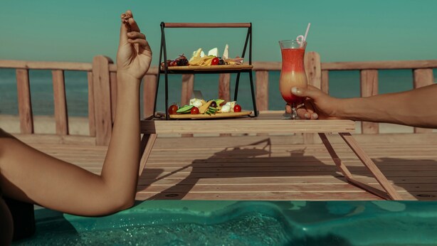 A wooden deck with a table set for a meal and drinks, overlooking a pool. - Cancun Sokhna Resort & Villas (Ataqah)