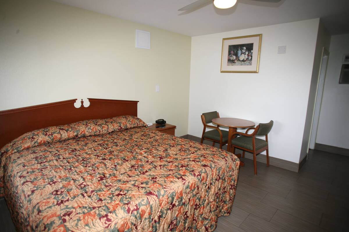 A hotel room with a large bed, a small table with two chairs, and a ceiling fan.