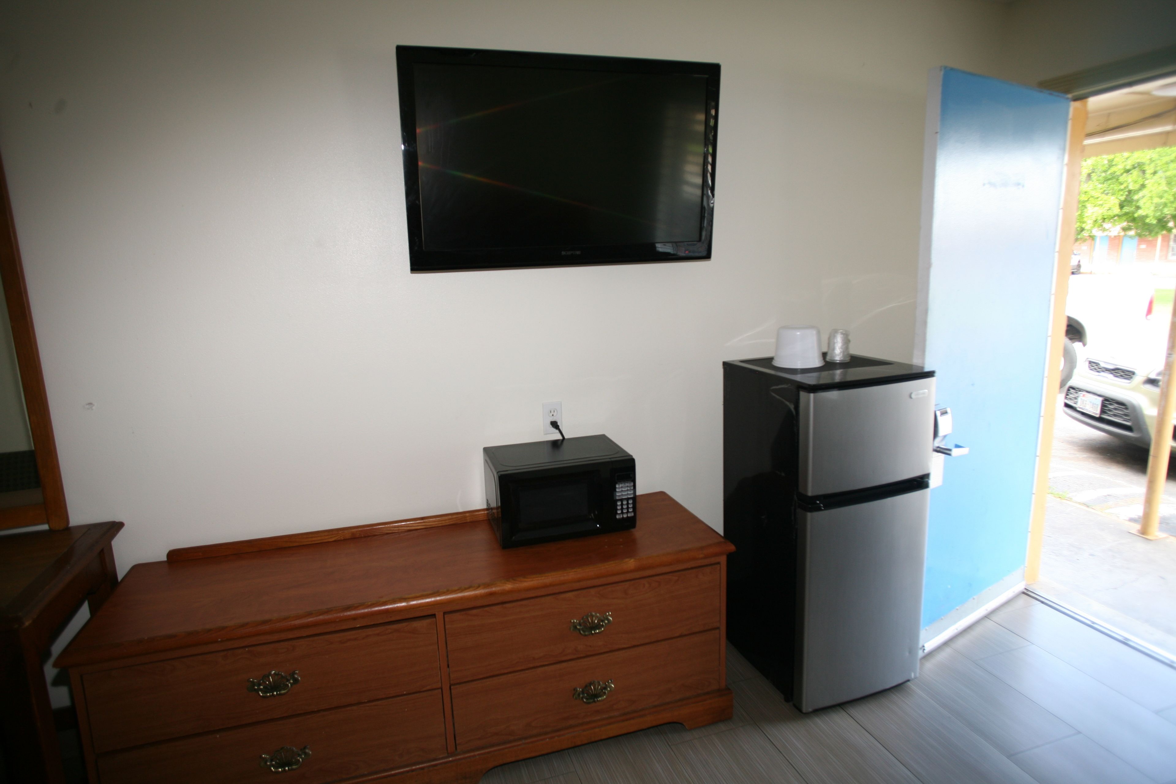 A kitchenette with a microwave, refrigerator, wooden dresser, and a flat-screen TV mounted on the wall.