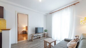 Ein modernes Wohnzimmer mit einem grauen Sofa, einem Holztisch und einem Fernseher auf einem Holzständer.