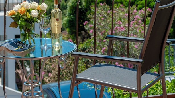 Ein Balkon mit Tisch, Stuhl und einer Weinflasche, mit Blick auf die Küste, wo Boote und viel Grün zu sehen sind.