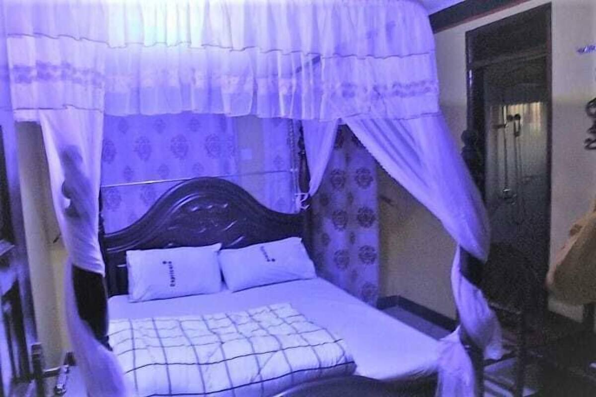 Uma cama de solteiro com dossel, cabeceira de madeira e papel de parede estampado.