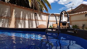 A swimming pool with a clear blue water surface, surrounded by a brick wall with a tiled roof and a palm tree. - Two steps from Toledo and Las Barrancas de Burujón (Escalonilla)
