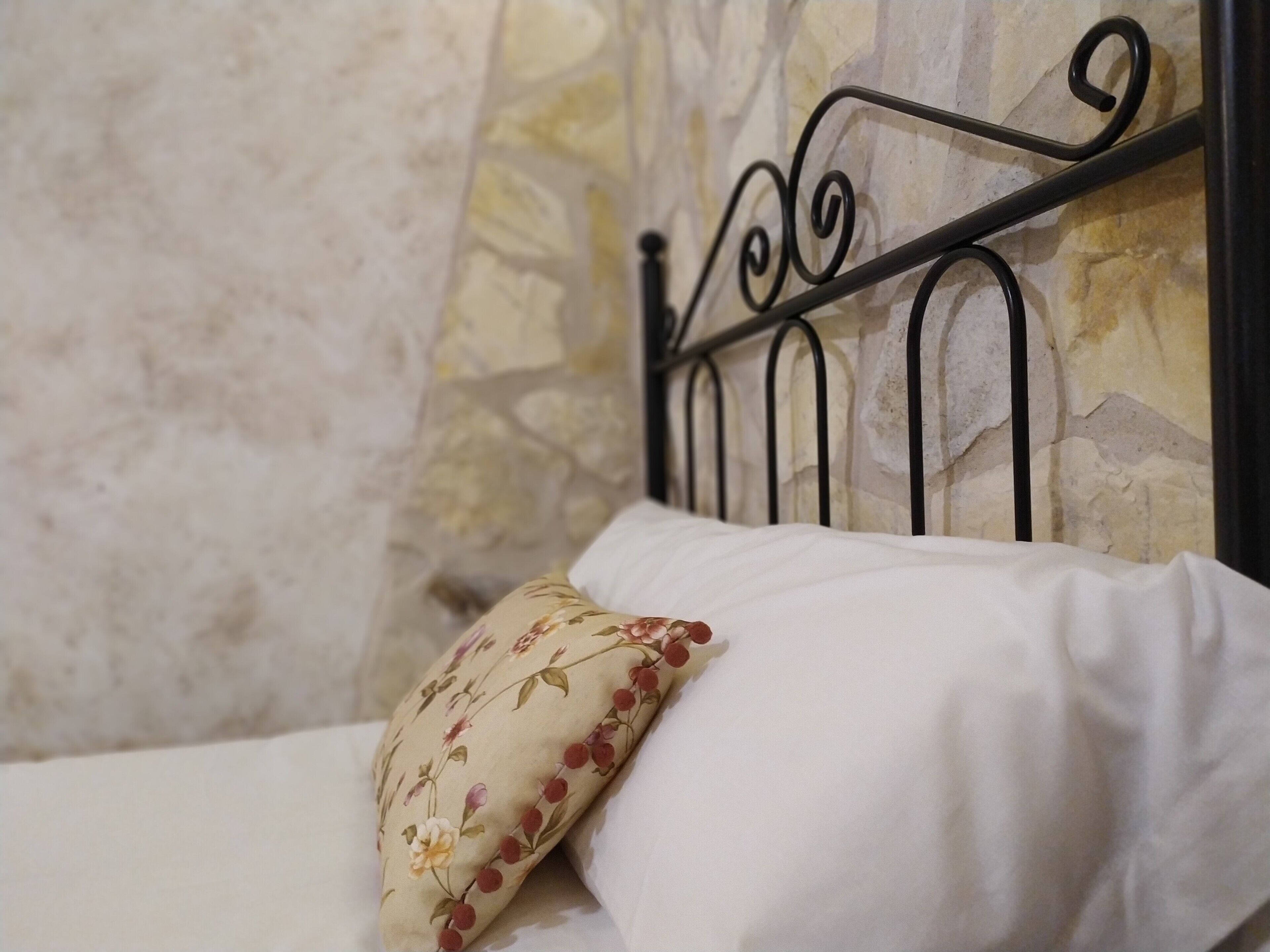 Un letto con un cuscino floreale e una testiera in metallo, addossato a una parete in pietra.