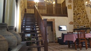 A rustic interior with a wooden staircase, stone walls, a television, and a dining area with checkered tablecloths. - Two steps from Toledo and Las Barrancas de Burujón (Escalonilla)