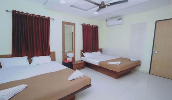 Una habitación de hotel con dos camas, cortinas rojas, ventilador de techo y aire acondicionado.
