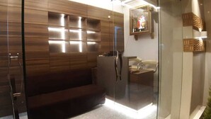 A modern bathroom with a glass shower enclosure, a wooden vanity, and a bench. - Rajhuns Deluxe Lodging (Kolhapur)