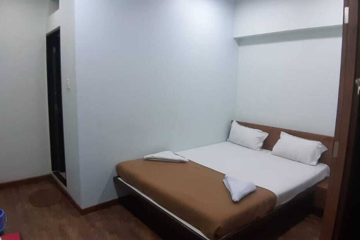 Ein kleines Zimmer mit einem Einzelbett, Holzboden, weißen Wänden und einer Tür links.