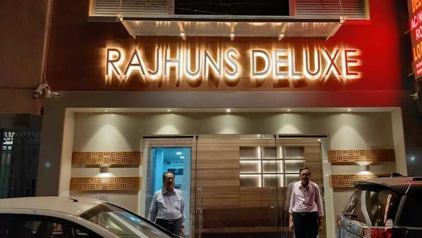 The exterior of Rajhuns Deluxe hotel with a prominent illuminated sign, a modern entrance, and a visible reception area. - Rajhuns Deluxe Lodging (Kolhapur)