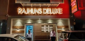 Exterior del hotel Rajhuns Deluxe, con un llamativo letrero iluminado, una entrada moderna y un área de recepción visible.