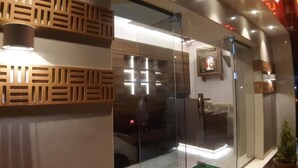A modern interior with a glass partition, a wooden decorative panel, and a framed picture on the wall. - Rajhuns Deluxe Lodging (Kolhapur)