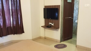 A room with a mounted TV, a door, and a small rug on the floor. - Hotel Bhagwati Lodging (Kolhapur)