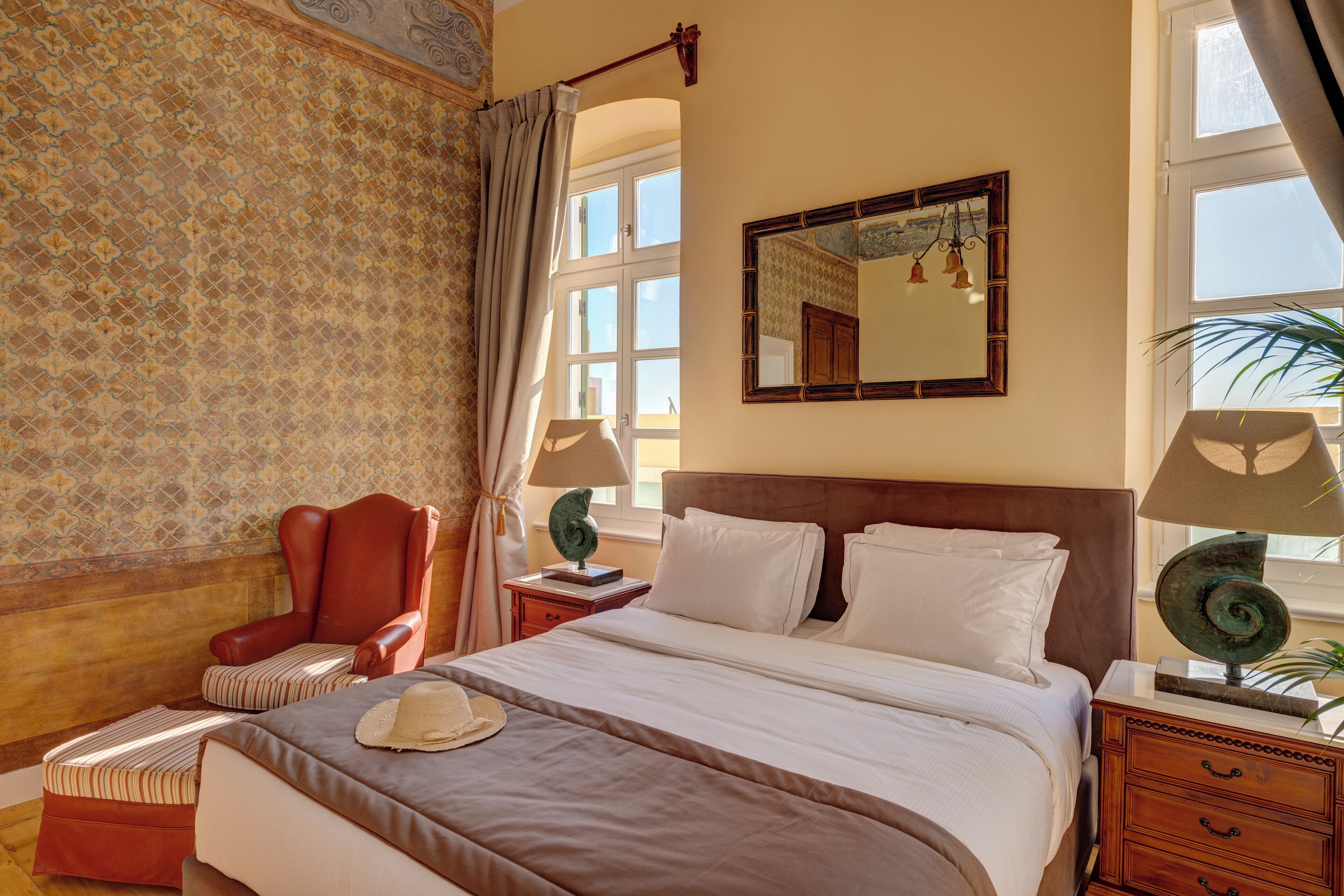 A neatly arranged bedroom with a large bed, a chair, a nightstand, and a mirror.