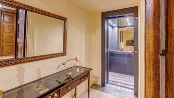 Um corredor com porta de madeira, espelho e mesa de vidro com abajur de latão.