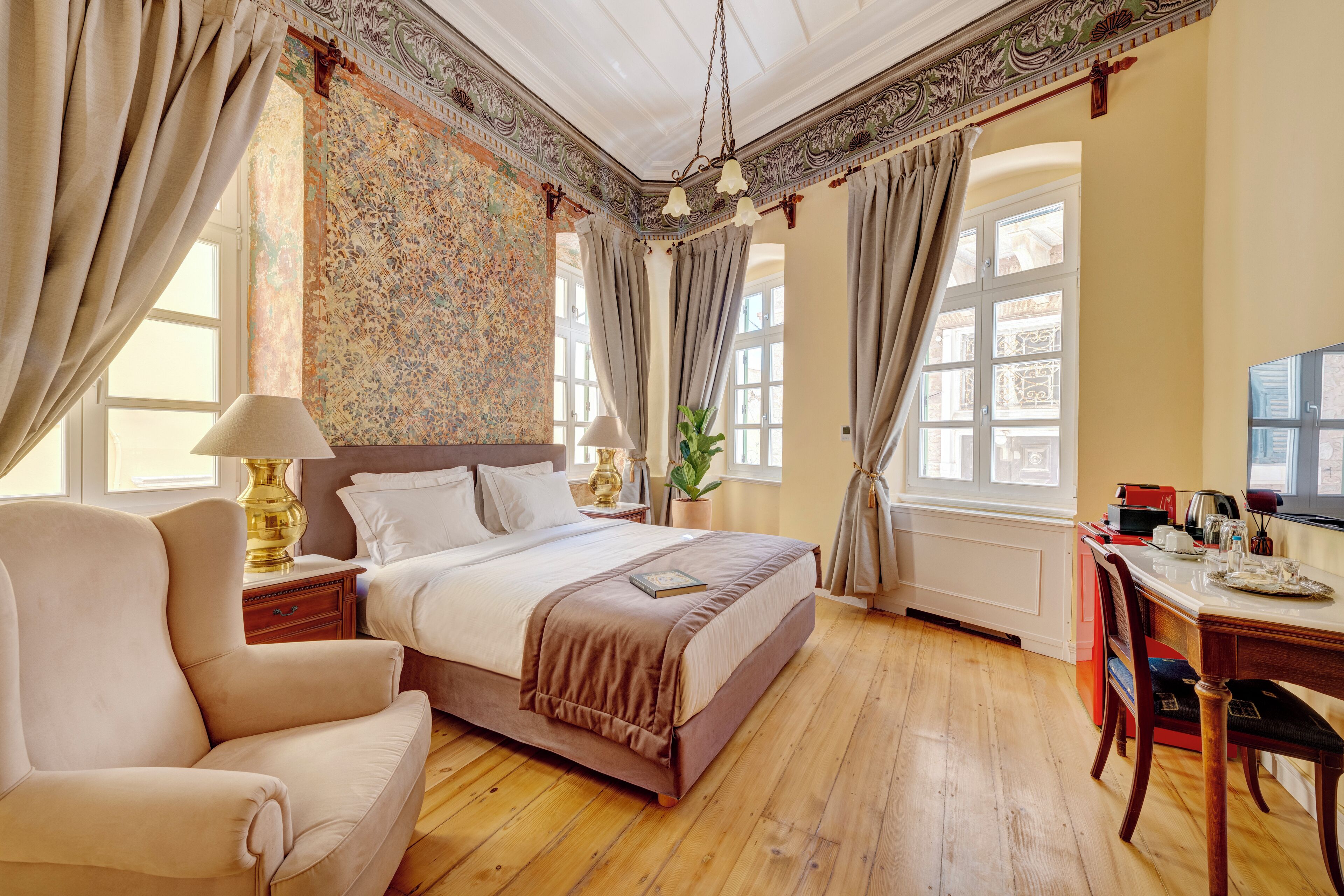 Ein geräumiges Schlafzimmer mit einem großen Bett, einer Sitzecke mit einem Sessel, einem Esstisch und Blick auf die Stadt durch große Fenster.
