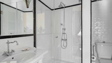 Un baño moderno con piso de mármol blanco, ducha con cerramiento de vidrio, lavamanos blanco con espejo y un inodoro.