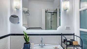 A modern bathroom with a white sink, a mirror, a potted plant, and a shower area.