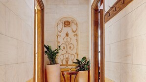 A hallway with marble walls, a wooden floor, and a large potted plant. - Palazzo Santa Maria - Historic Hotels of Europe (Syros)