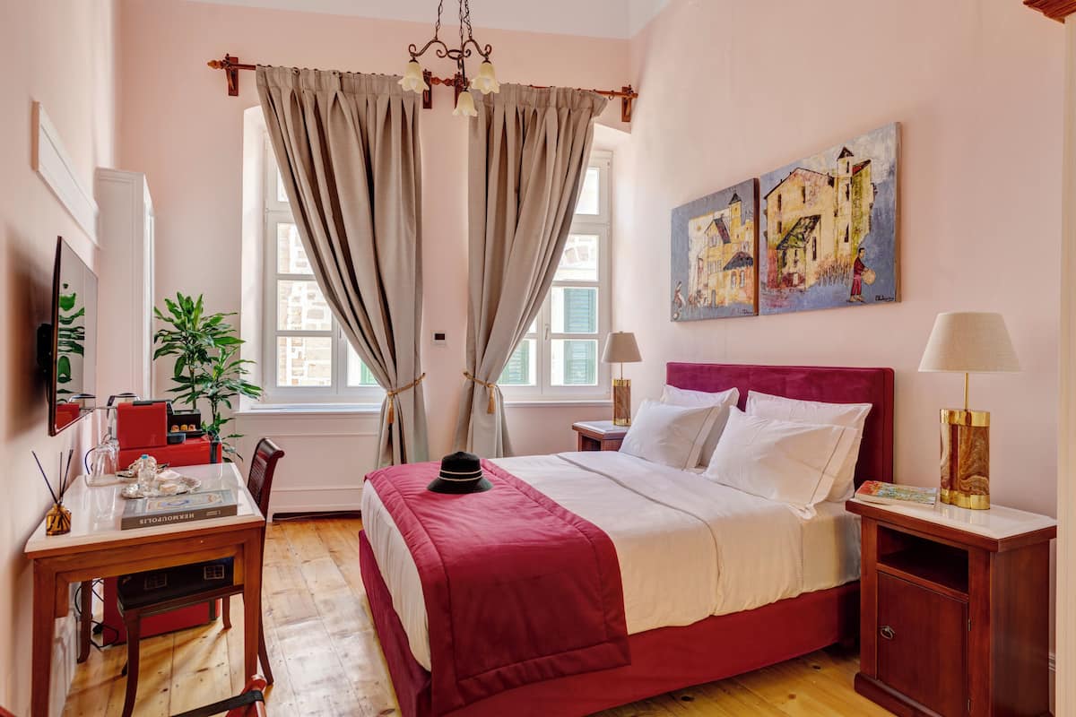 A bedroom with a bed, a desk, a chair, a lamp, and a painting on the wall.