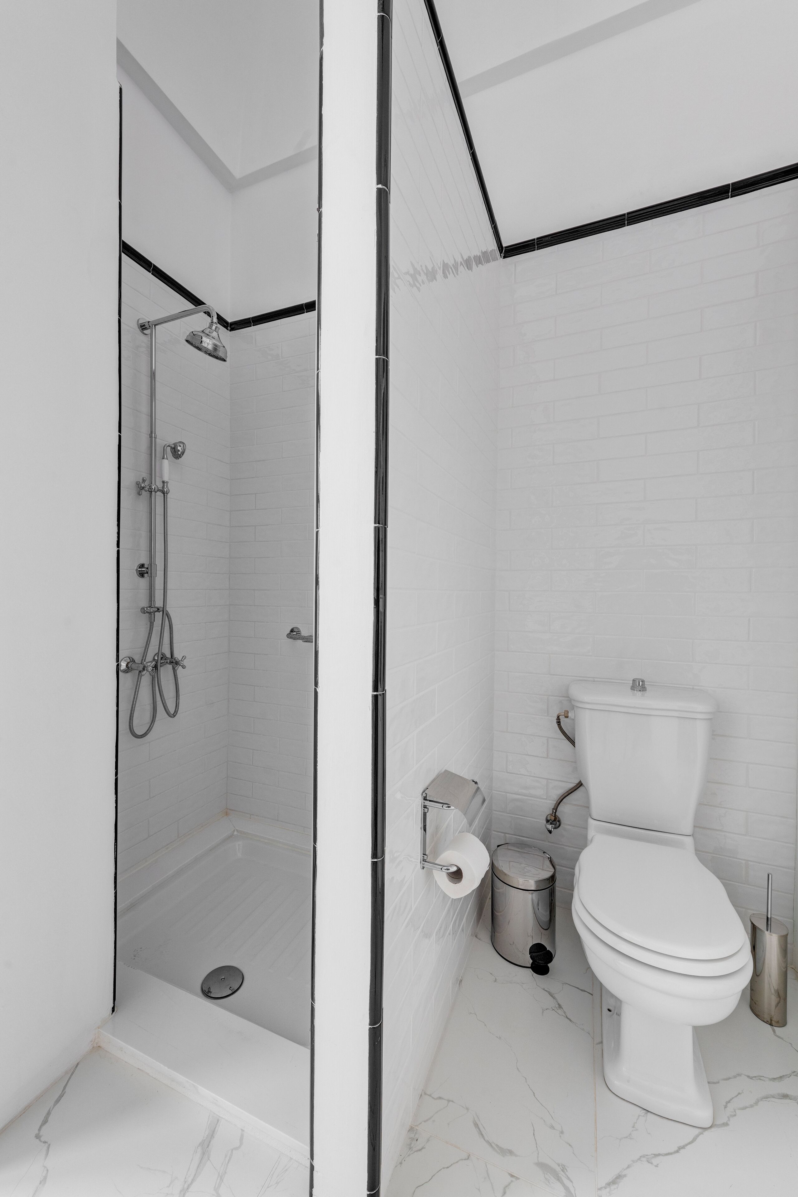 A modern bathroom with a glass-enclosed shower, white tiled walls, a toilet, and a marble floor.