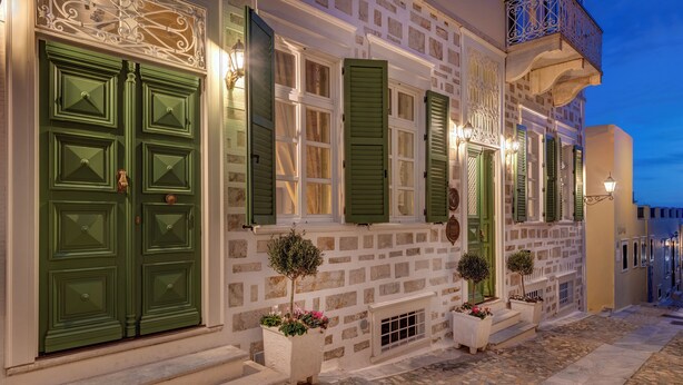 A traditional building with green shutters, stone walls, and a cobblestone street. - Palazzo Santa Maria - Historic Hotels of Europe (Syros)