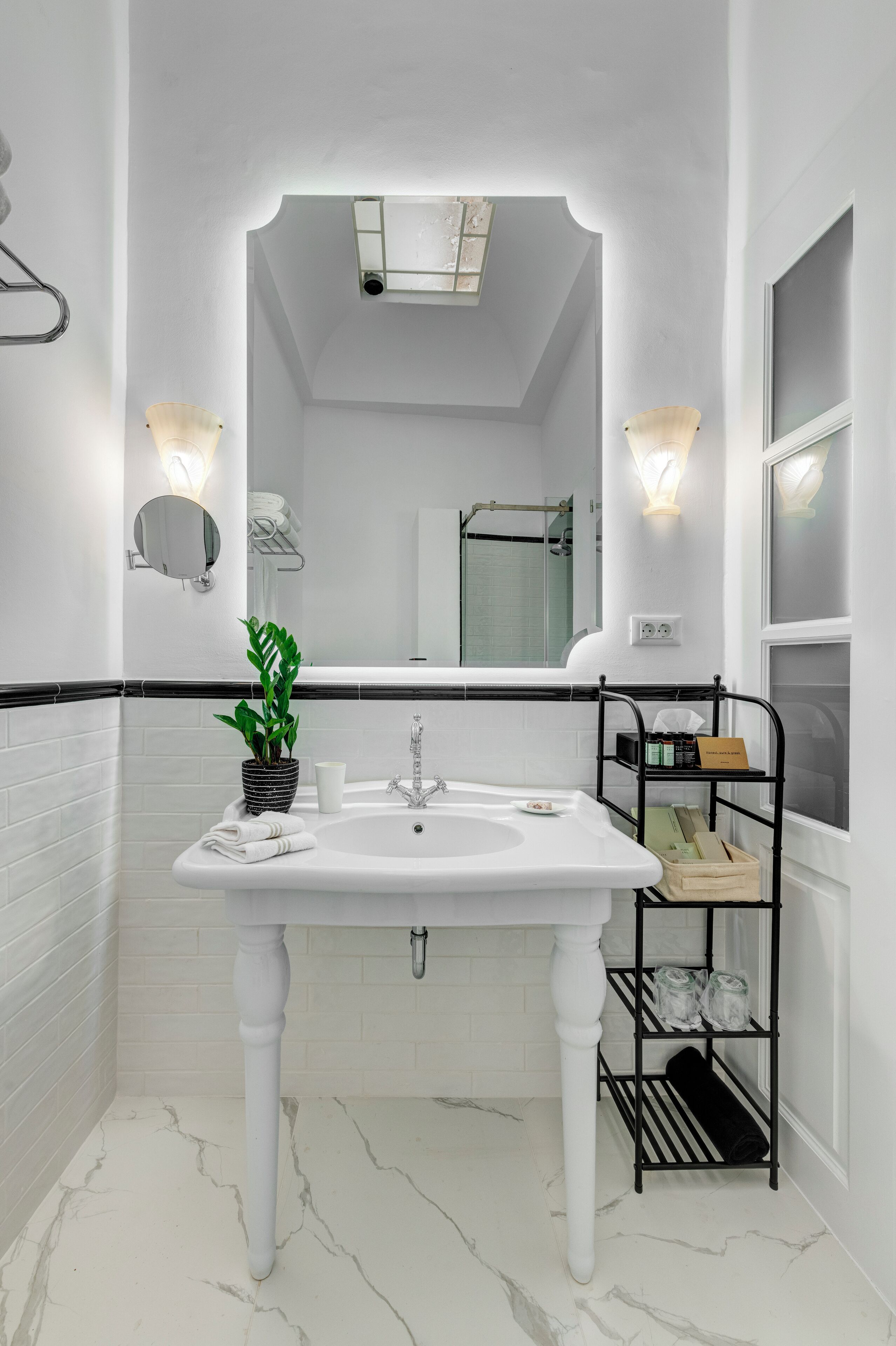 Ein modernes Badezimmer mit einem weißen Waschbecken, einer Topfpflanze und einem schwarzen Metallregal mit Pflegeprodukten.