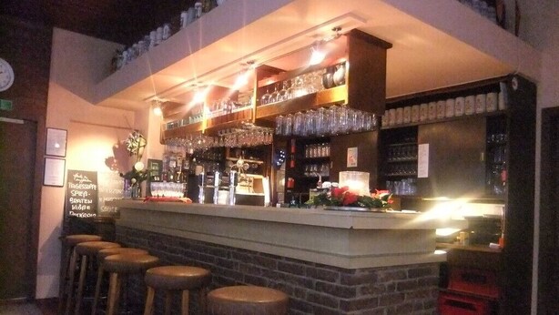 Een bar met krukken, glazen en flessen op de planken.
