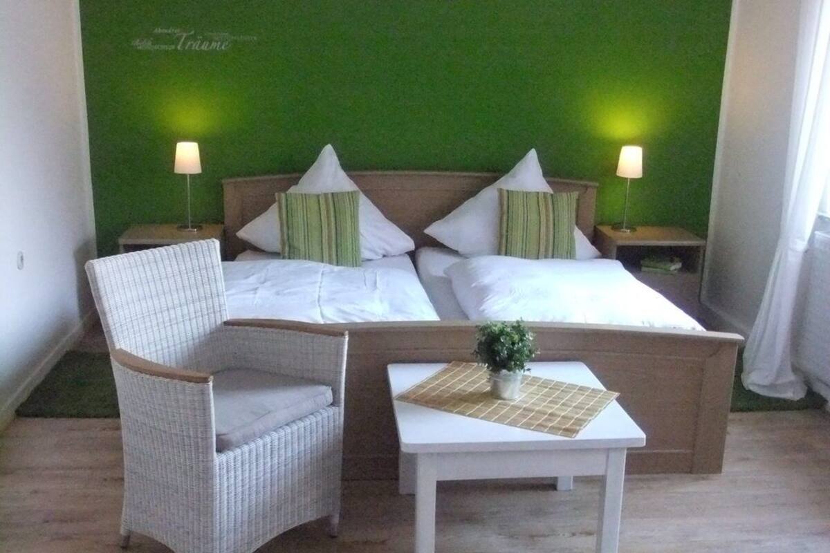 Ein Schlafzimmer mit einem Bett, zwei Nachttischen, einem Sessel und einem kleinen Tisch mit einer Pflanze.