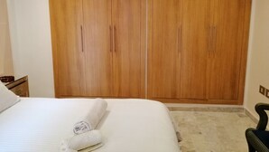 A bedroom with a large wooden wardrobe, a bed with white linens, and a small bedside table. - Superbe appartement avec Piscine (La Soukra)